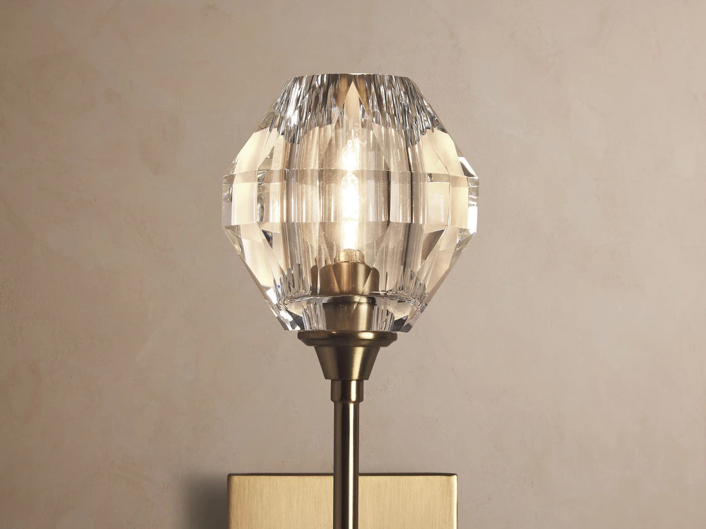Amoroso Sconce: brass-plated wall-mounted fixture with a long arm, topped by a faceted clear crystal element.
