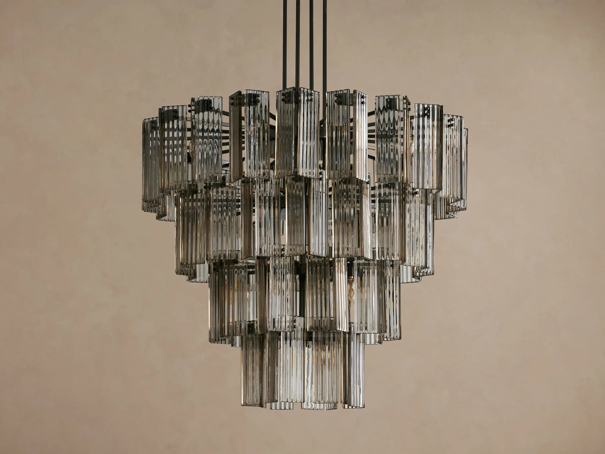 Delsie Round Chandelier with multiple tiers of fluted, smoky glass rods & warm-glowing lights, suspended from a dark metal frame.