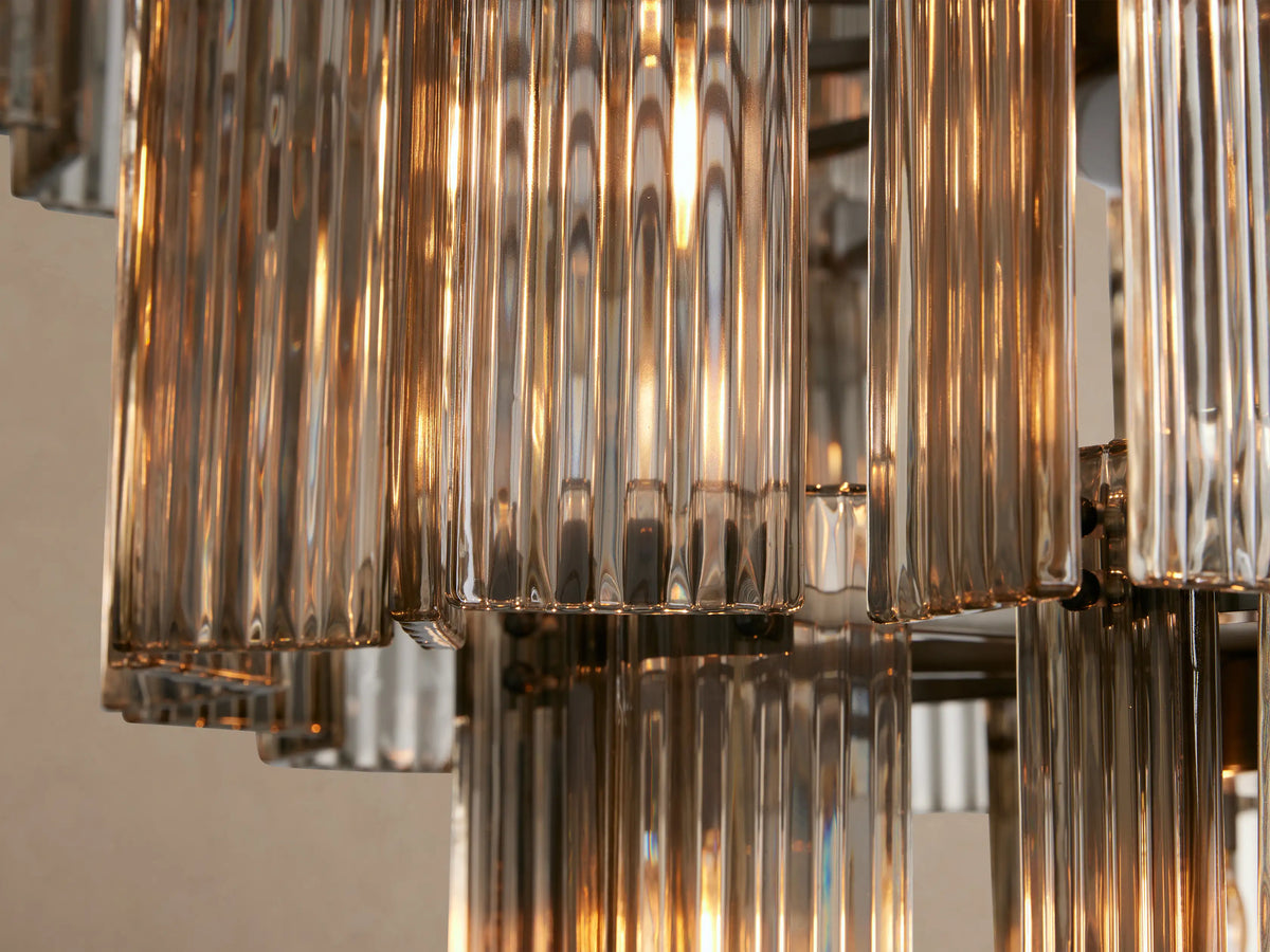 Delsie Round Chandelier, multi-tiered with vertical fluted smoky glass rods and a dark metal frame, hanging against a beige wall.