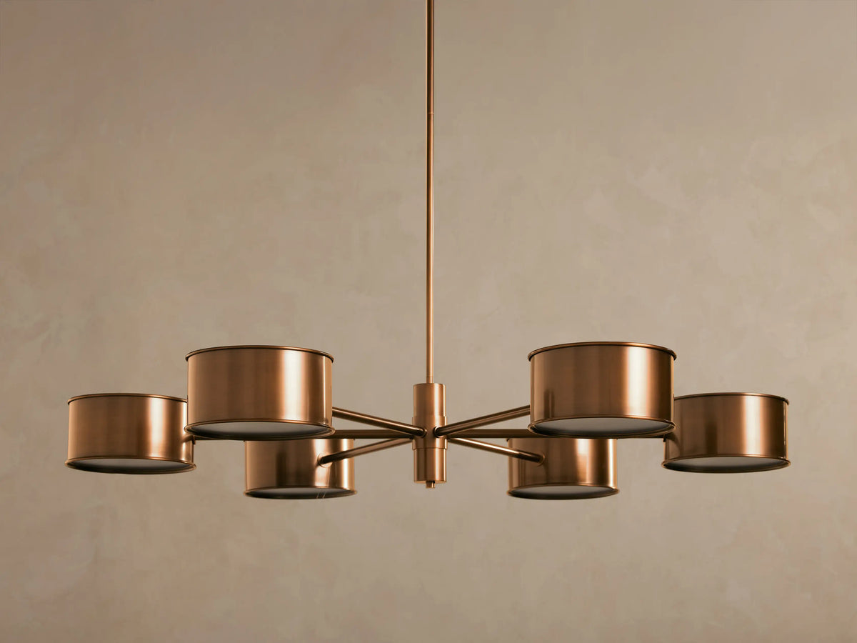 Daphne Metal Round Chandelier in warm bronze with six cylindrical shades, hanging from a rod, lights illuminated.