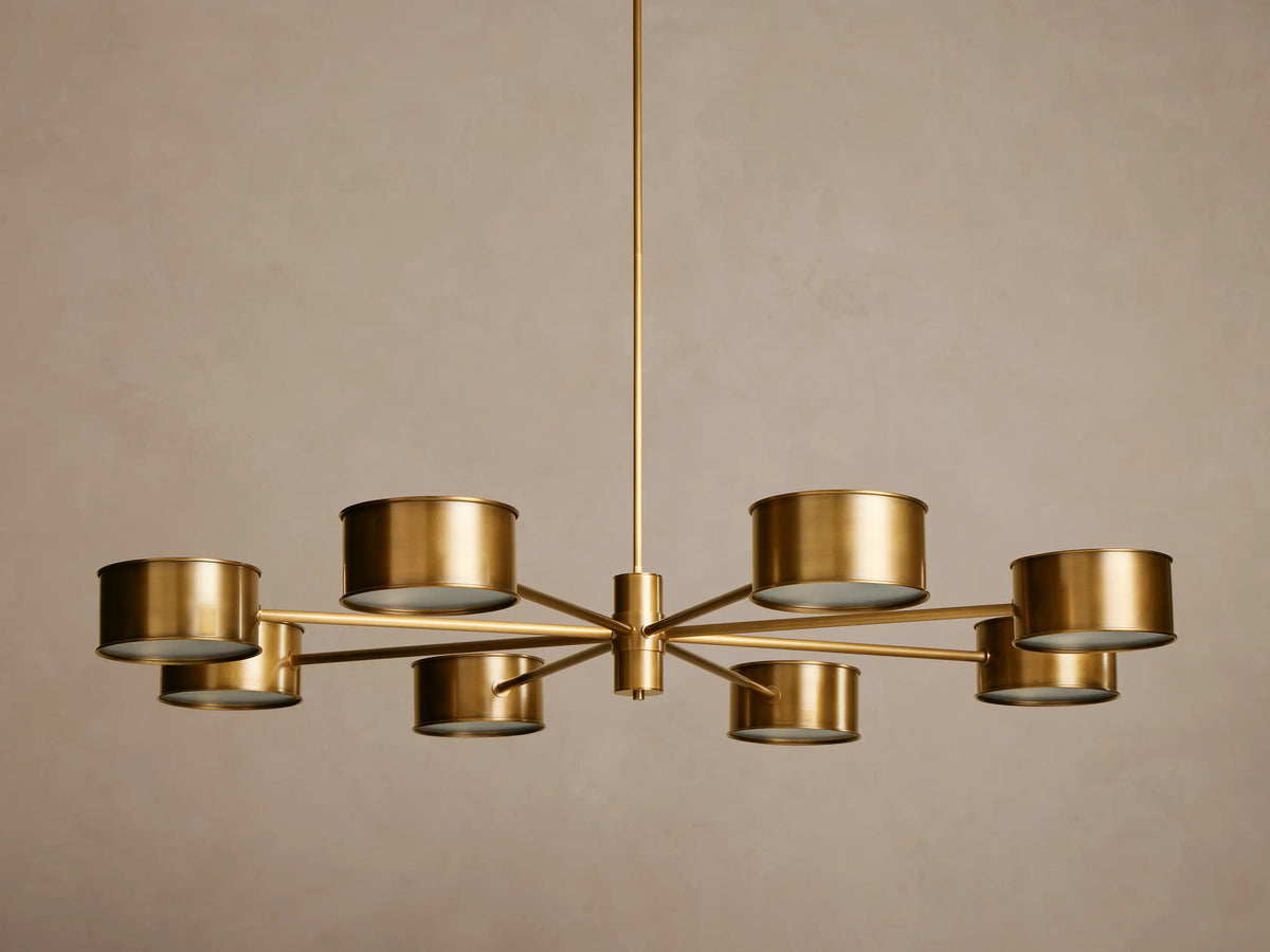 Daphne Metal Round Chandelier in gold/brass with eight drum-shaped shades emitting warm light, hanging from a central rod.