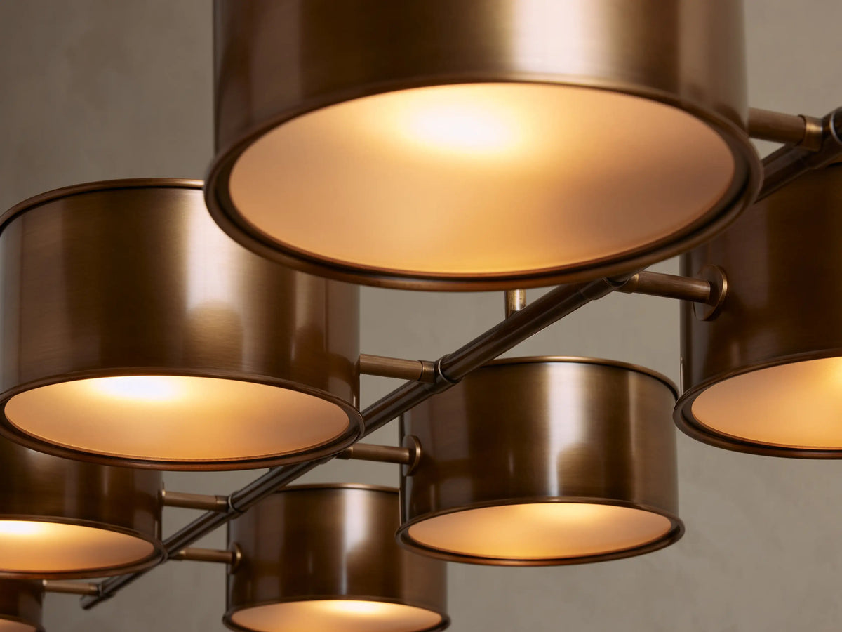 Daphne Metal Linear Chandelier: 8 antique brass cylindrical shades with white diffusers, suspended horizontally from rods.