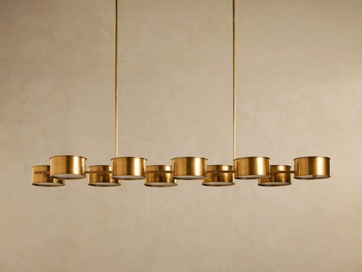 Daphne Metal Linear Chandelier: Antique brass fixture, 10 illuminated cylindrical shades arranged horizontally, suspended.