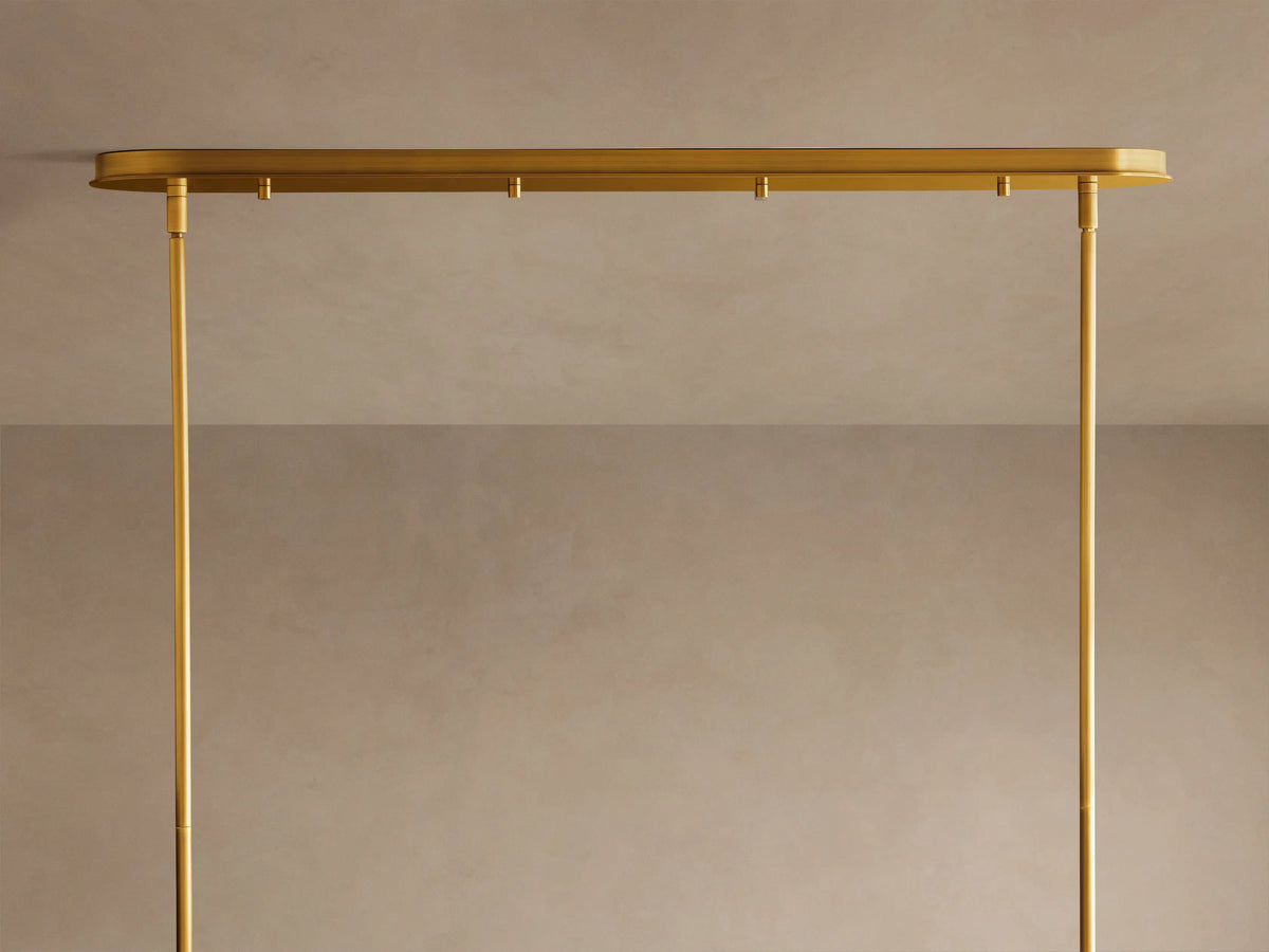 Close-up of Daphne Metal Linear Chandelier. Multiple antique brass drum shades glow warmly, some illuminated.