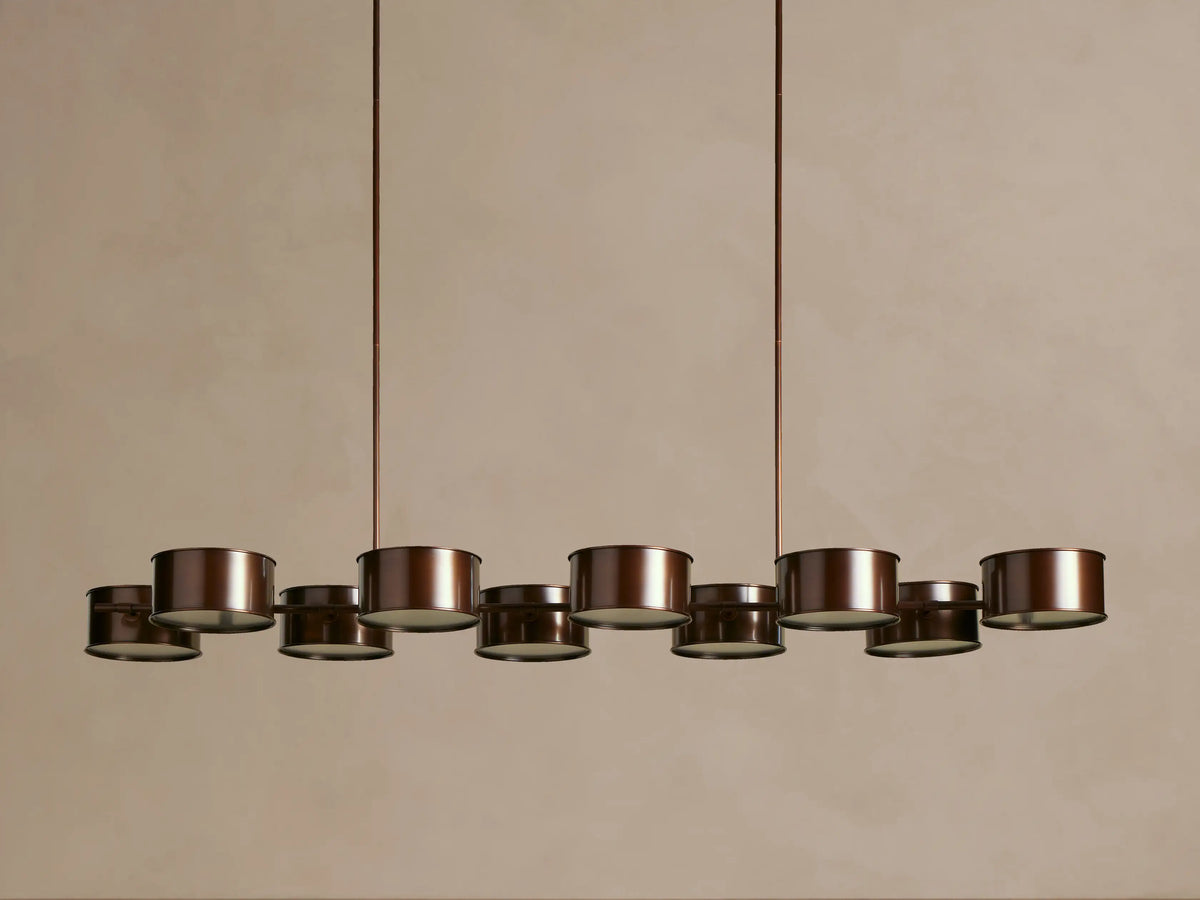 Daphne Metal Linear Chandelier with 9 dark bronze drum shades, emitting warm light, hanging from rods.