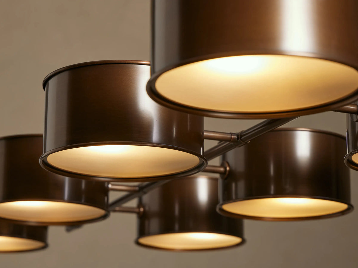 Daphne Metal Linear Chandelier: 10 warm bronze cylindrical shades suspended linearly from two bronze rods against a light wall.