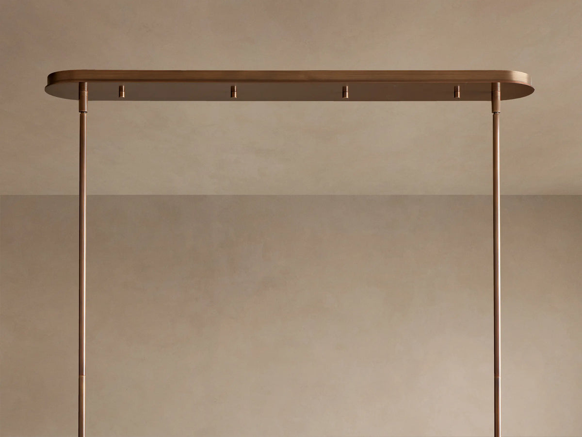 Close-up of a Daphne Metal Linear Chandelier. Several warm bronze metal shades emit bright light, one tilted to show its interior.