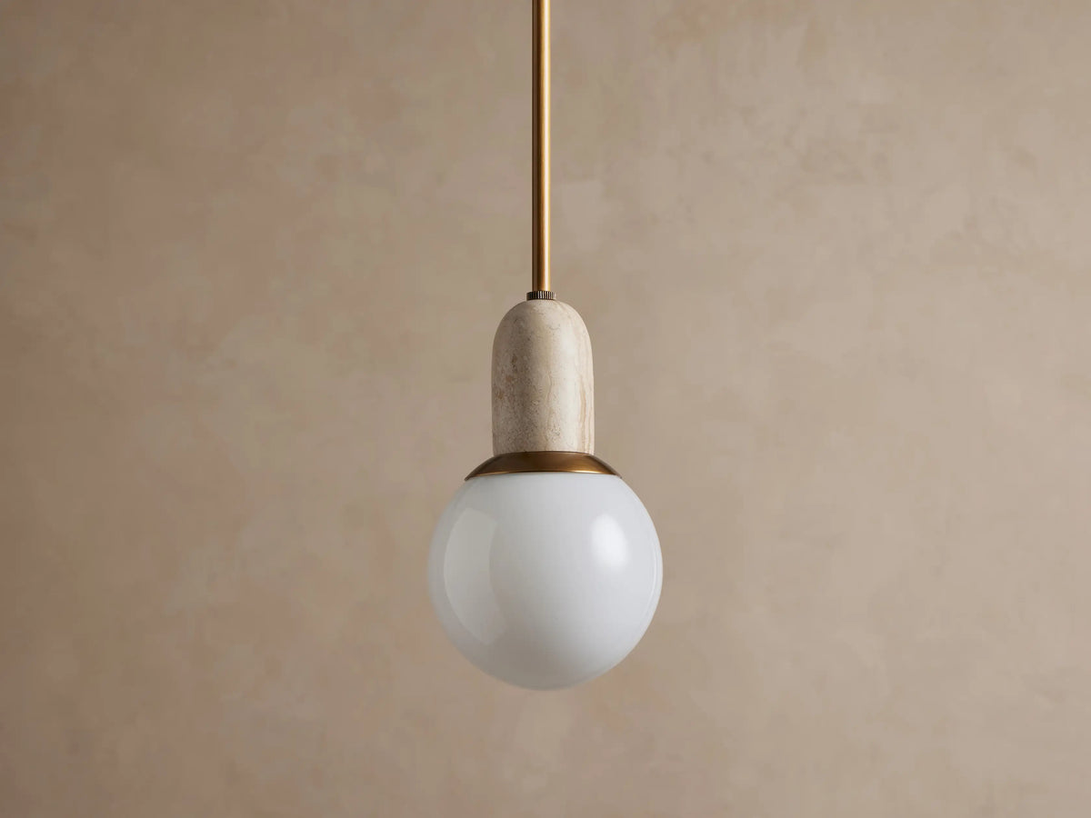 Christie Pendant light hanging. Features a brass rod, natural gray stone cap, and a glowing spherical milk glass shade.