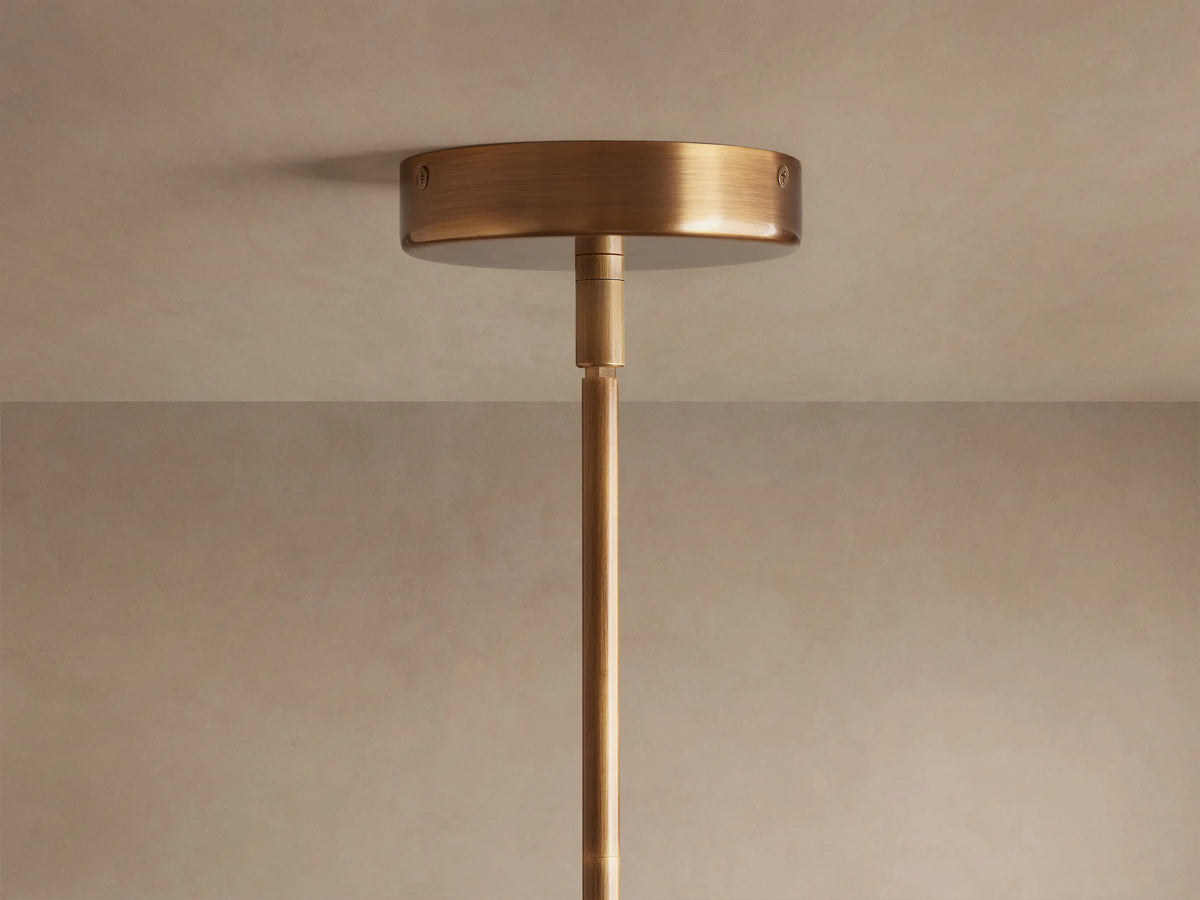 Christie Pendant: Close-up of beige striated natural stone, brass collar, and glowing milk glass shade hanging.