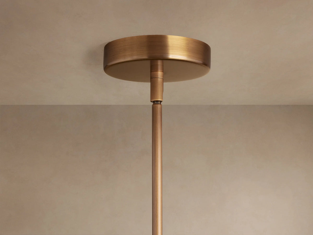 Christie Pendant close-up: black marbled stone column, brushed brass ring, and smooth white milk glass globe shade.