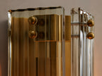 Delsie Sconce, a vertical fluted glass and burnished brass wall light, mounted on a grey wall next to a dark-framed mirror.