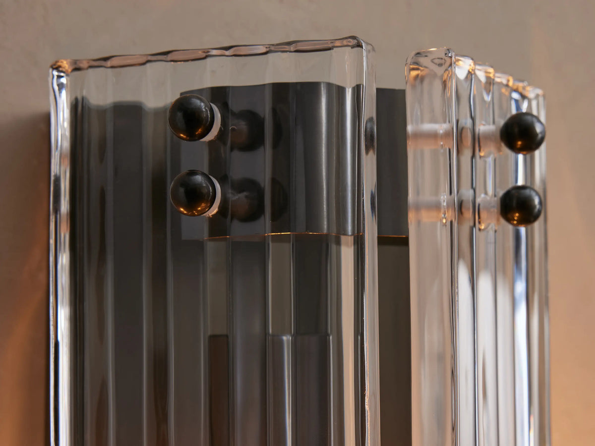 Delsie Sconce: vertical, rectangular, black steel base with fluted smoky & clear glass, lit by two bulbs, on a wall.