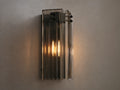 Delsie Sconce: Vertical light with ribbed smoky glass, dark metal frame, and two glowing bulbs, on a light wall beside a mirror.