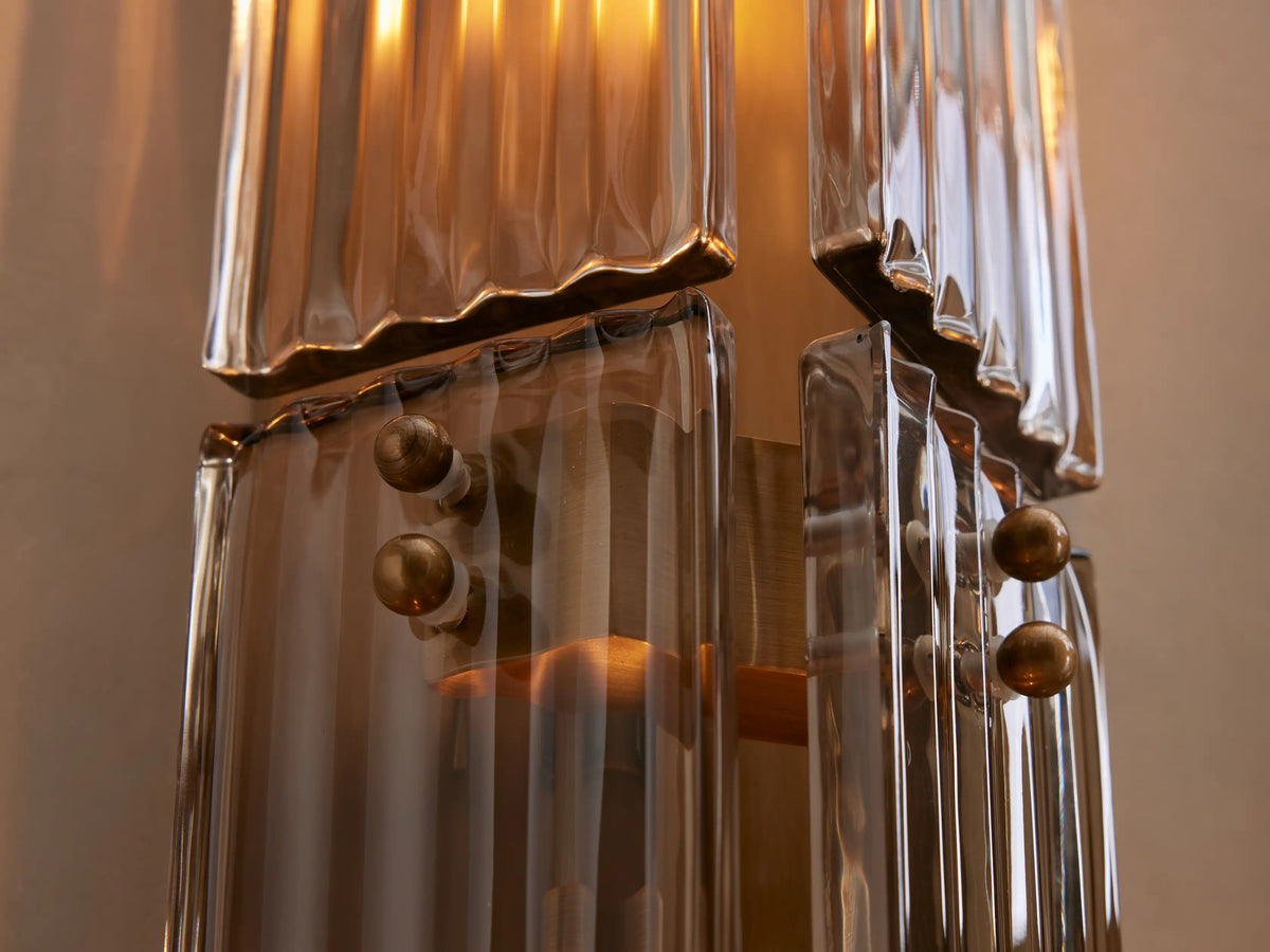 Delsie Double Sconce, vertical, burnished brass/bronze with clear glass rods & two bulbs, on a light wall next to a mirror.