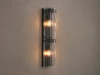 Vertical Delsie Double Sconce, dark frame with two illuminated bulbs behind ribbed clear glass, mounted on a wall near a mirror.