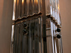Delsie Double Sconce, vertical, clear fluted glass panels, dark bronze base, visible bulbs, on a light wall beside a round mirror.