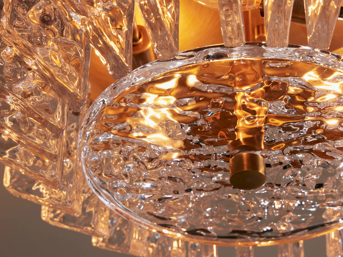 Liliana Flush Mount: close-up, angled view of a brass flush mount light with clear, textured glass panels on a beige ceiling.