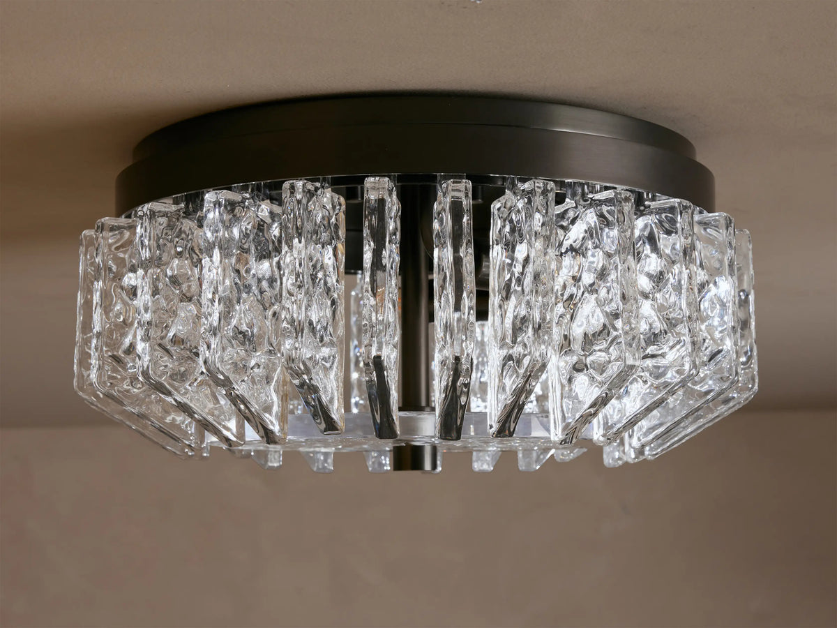 Liliana Flush Mount with a dark metal base and textured clear glass panels glowing with warm light, mounted on a ceiling.