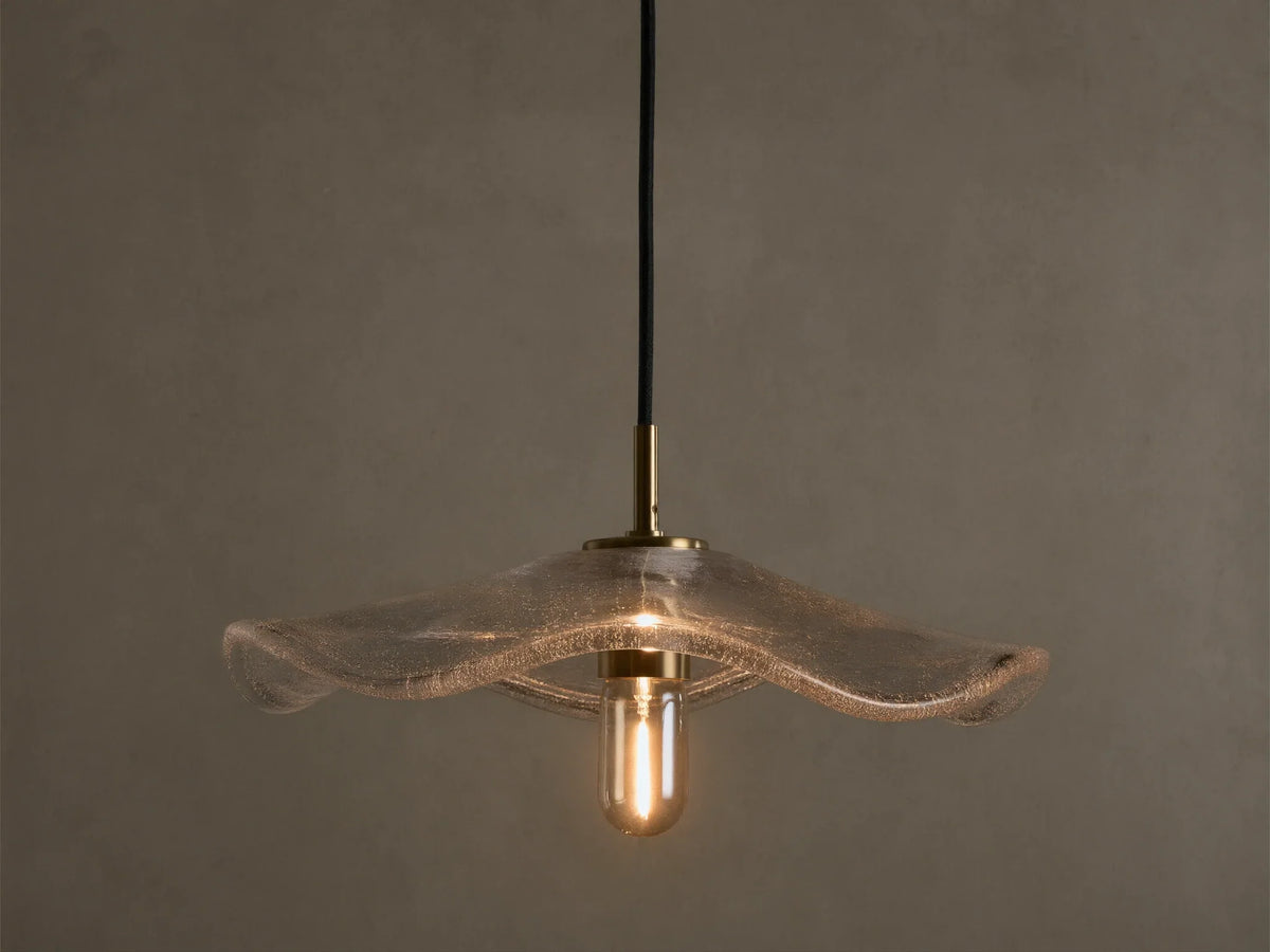 Front view of a clear wavy glass pendant light with a brass fixture and an exposed filament bulb, hanging from a black cord.