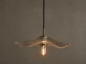 Front view of a clear wavy glass pendant light with a brass fixture and an exposed filament bulb, hanging from a black cord.