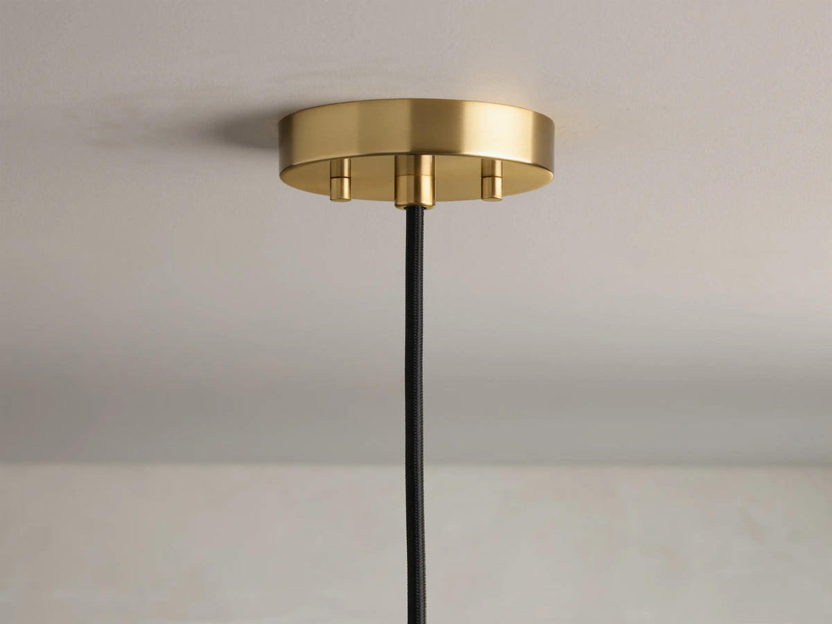 Close-up of the round, brushed brass ceiling canopy with three visible gold screws and a black braided cord.