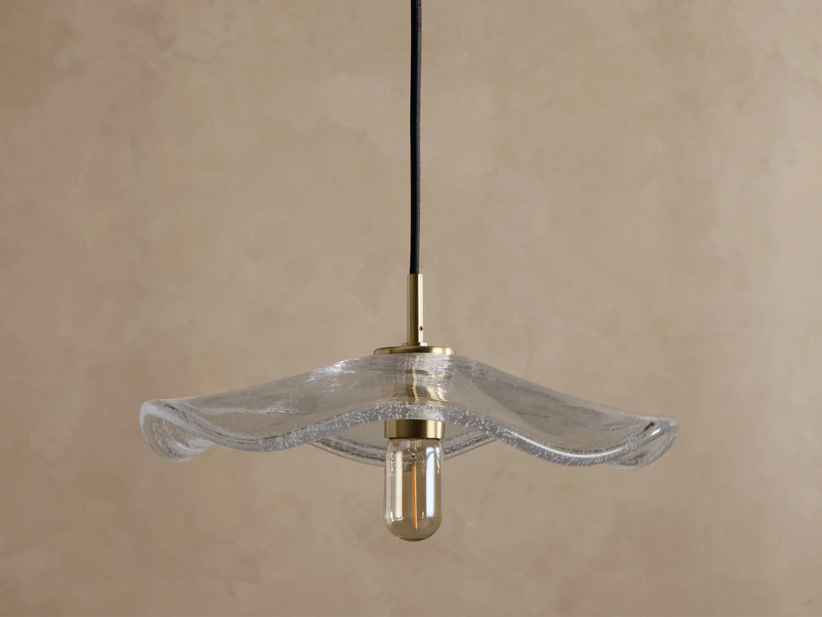 Front view of a clear wavy glass pendant light with a brass fixture and an exposed filament bulb, hanging from a black cord.