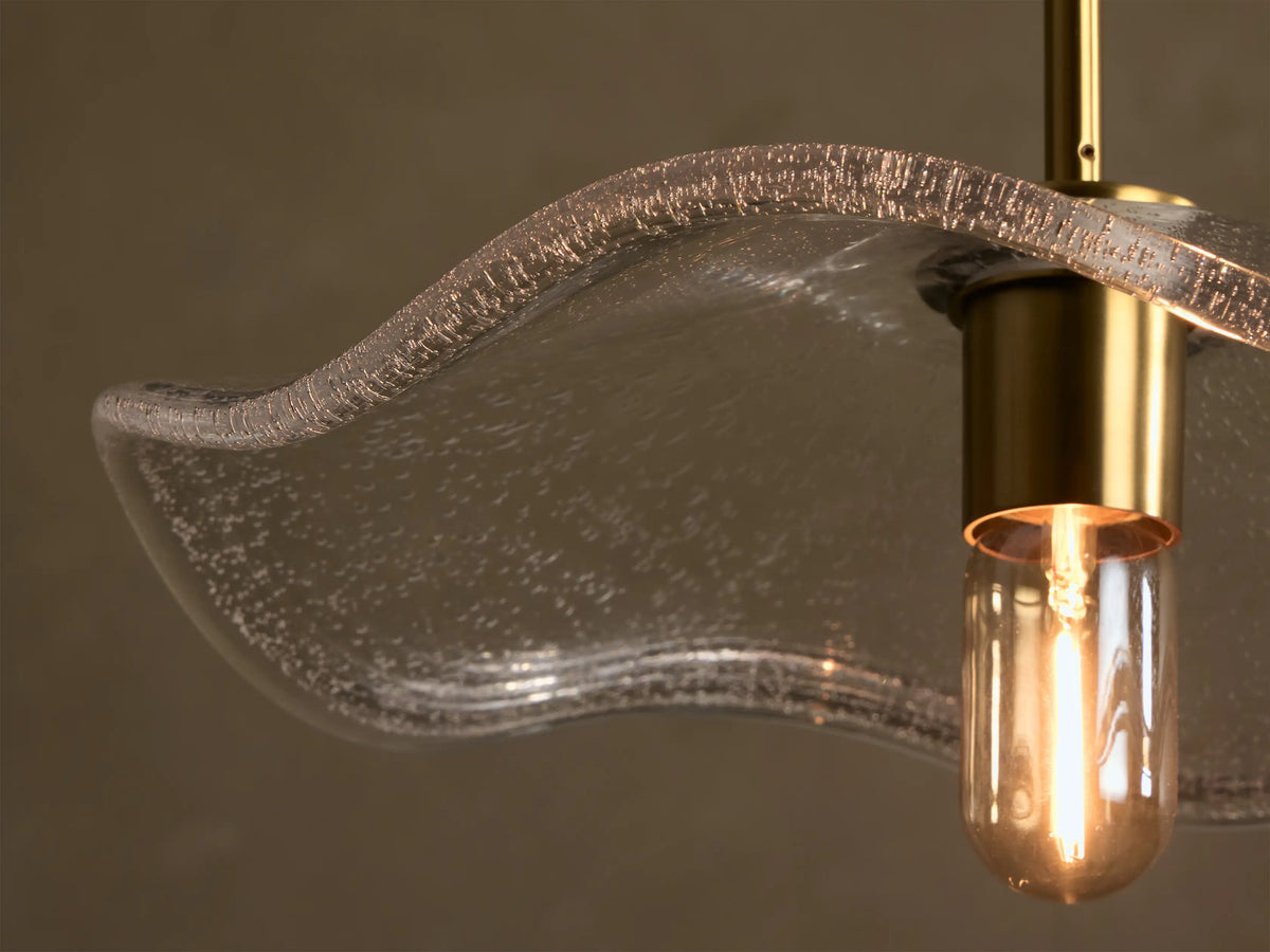 Front view of the clear ripple-effect glass pendant light, with a brass fitting, black fabric cord, and exposed filament bulb.