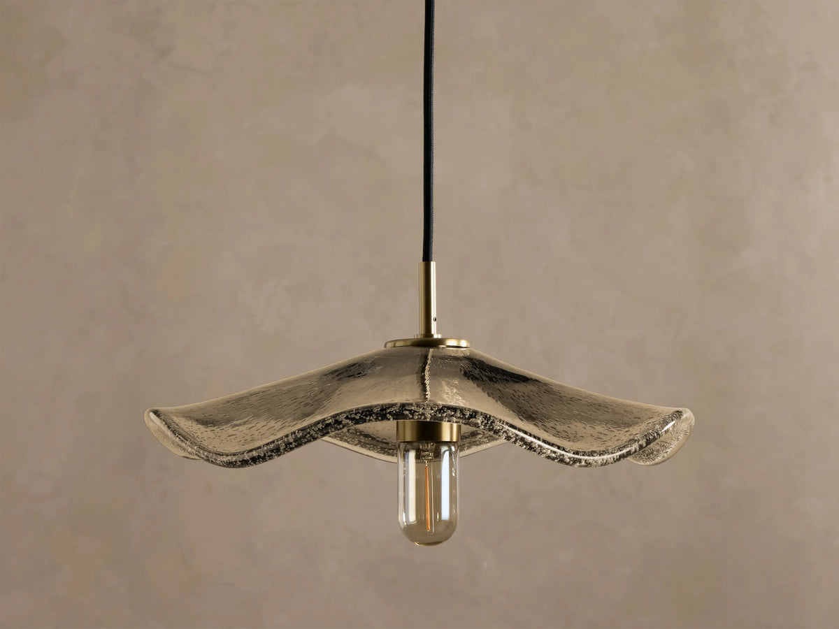 Close-up of a pendant light with a textured, iridescent antique glass shade, brass stem, and a warm-glowing filament bulb.
