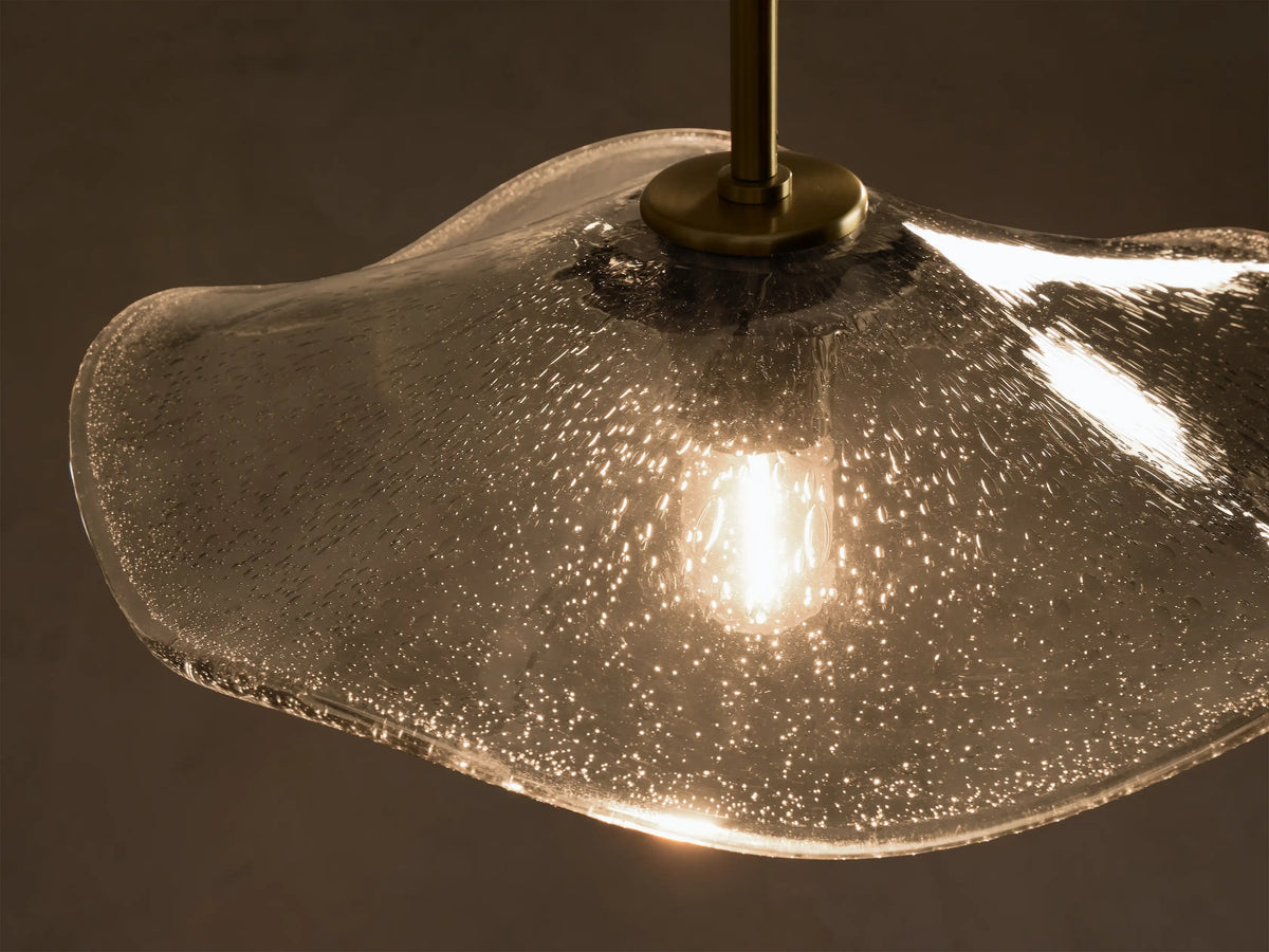 Front view of a wavy, textured smoky glass pendant light with brass hardware, an exposed filament bulb, and black cord.