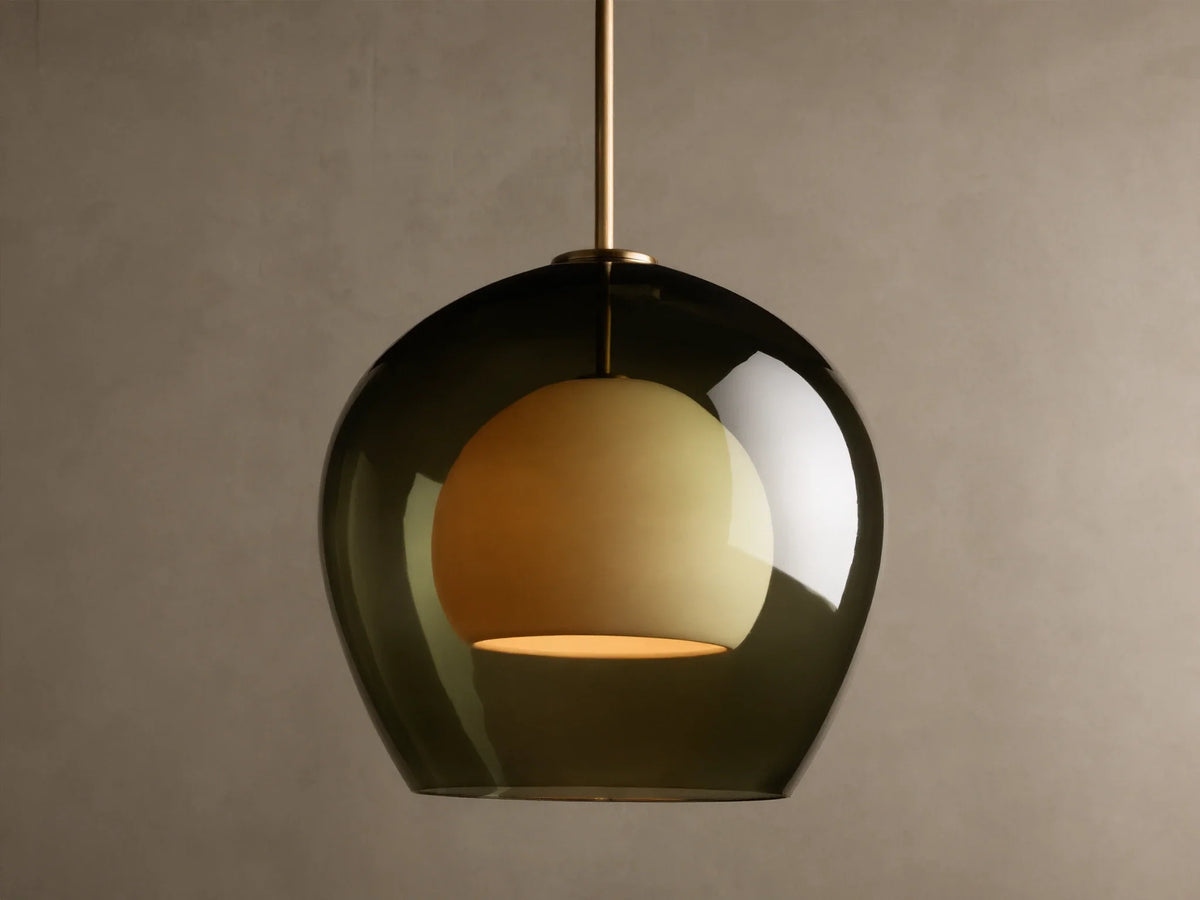 Front view of the Romy Pendant, featuring a dark green glass outer shade, an illuminated spherical cream inner diffuser, and a brass rod.