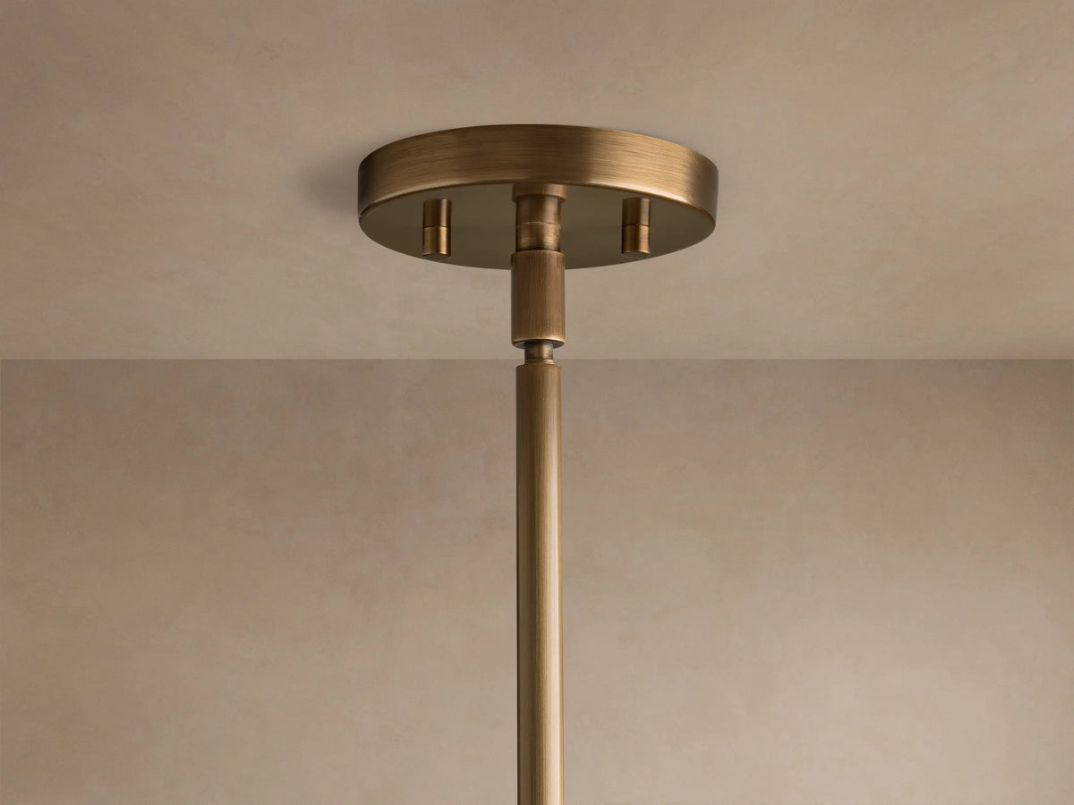 Close-up of the round warm brass ceiling mount and upper rod of the Romy Pendant.
