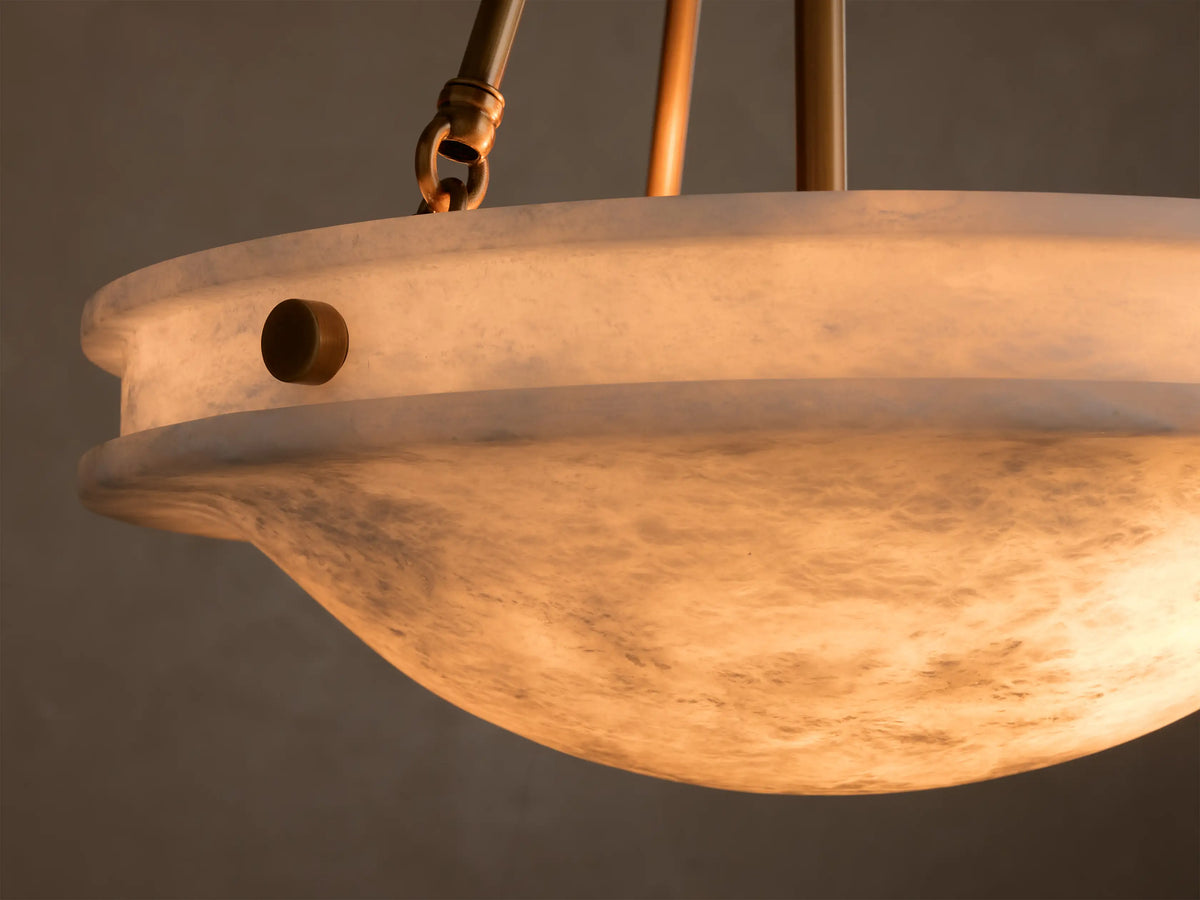 Close-up of the alabaster Edith Pendant's shade, glowing warmly, revealing natural marbling and a round brass button detail.