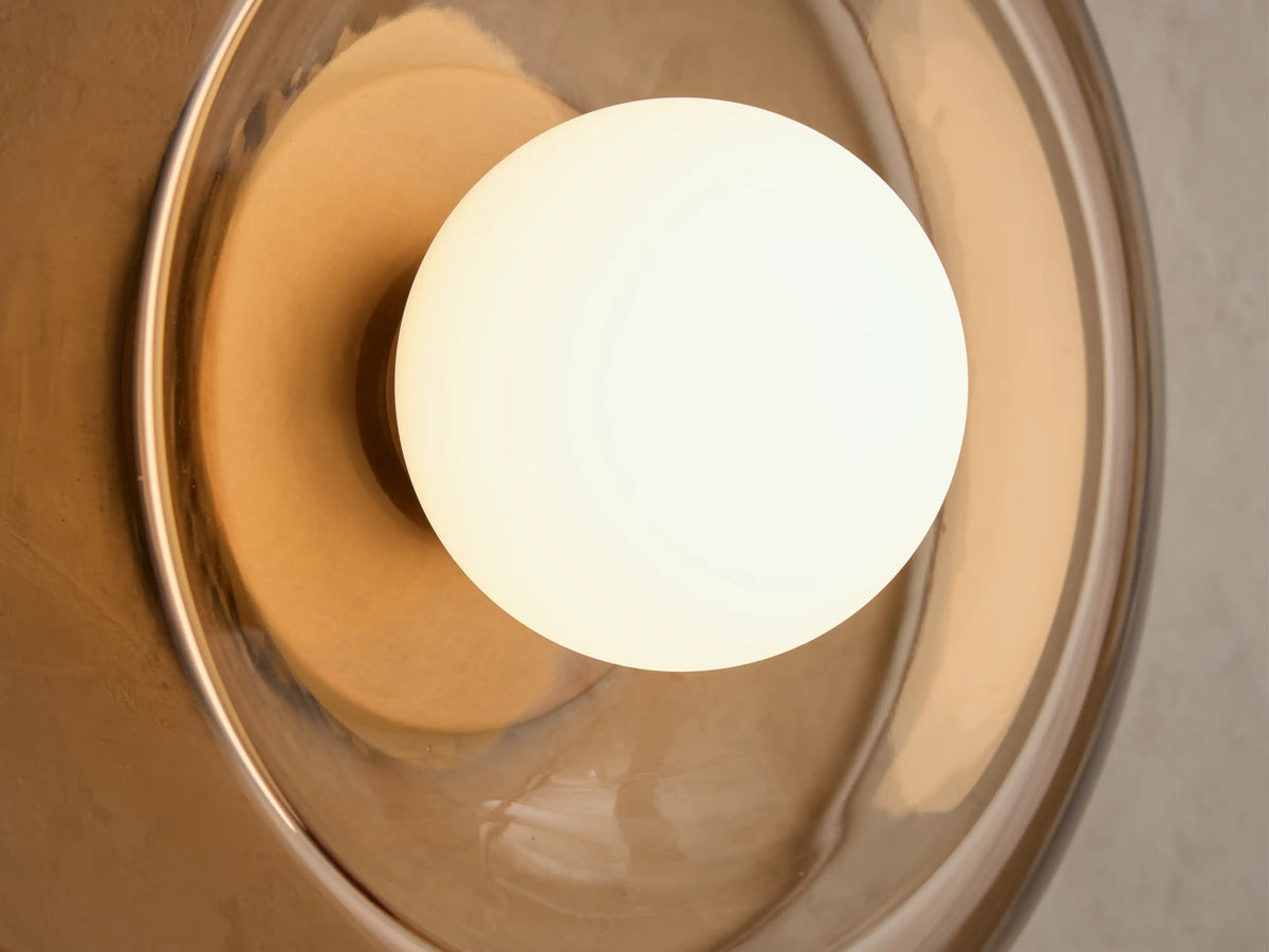Close-up of a white spherical light bulb recessed into a wavy, translucent amber glass wall light fixture.