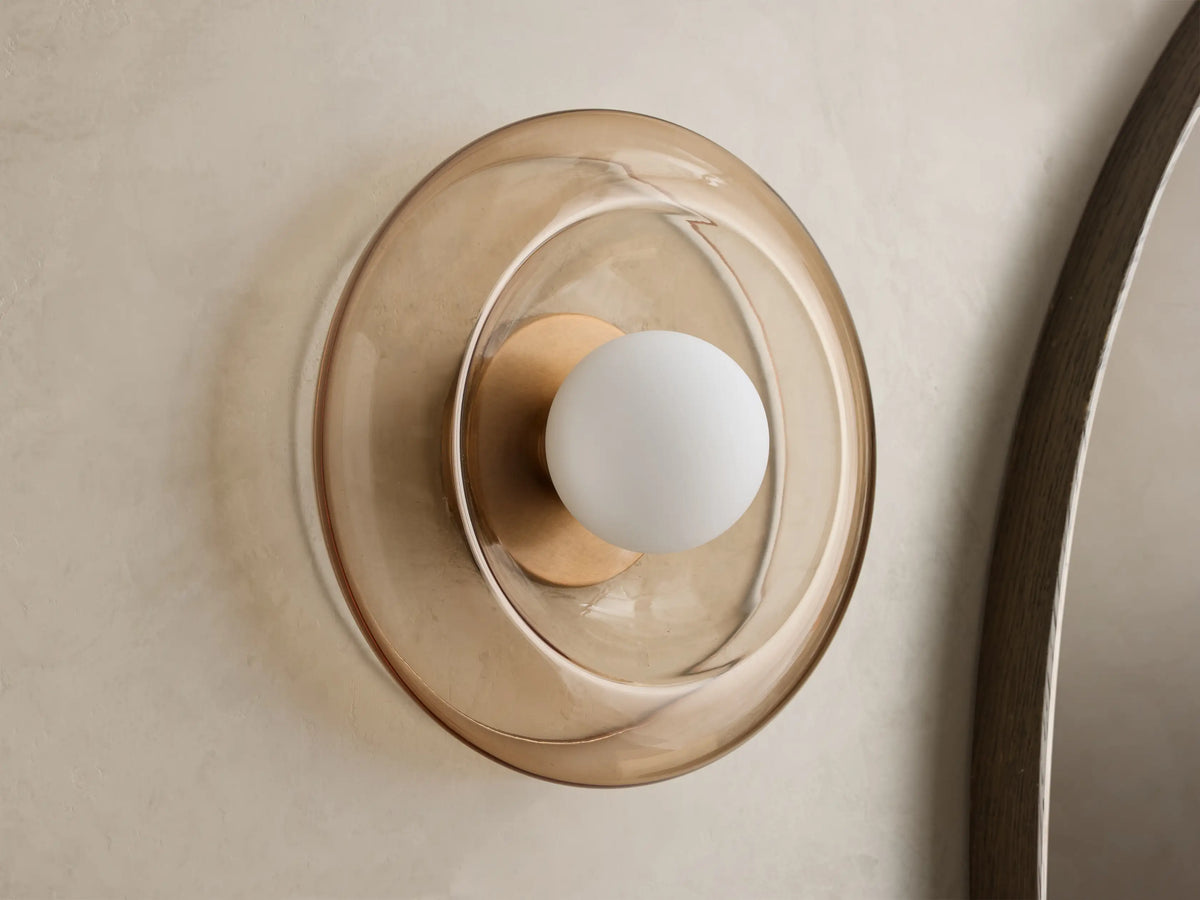 Front view of a wall sconce with a sculpted round amber glass shade, a brass-toned base, and a white globe bulb.