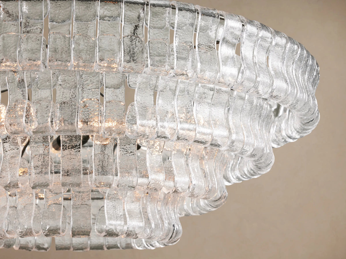 Angled view of Ghiaccio Round Chandelier. Clear, textured glass pieces form layered, wavy rings, glowing with warm light.