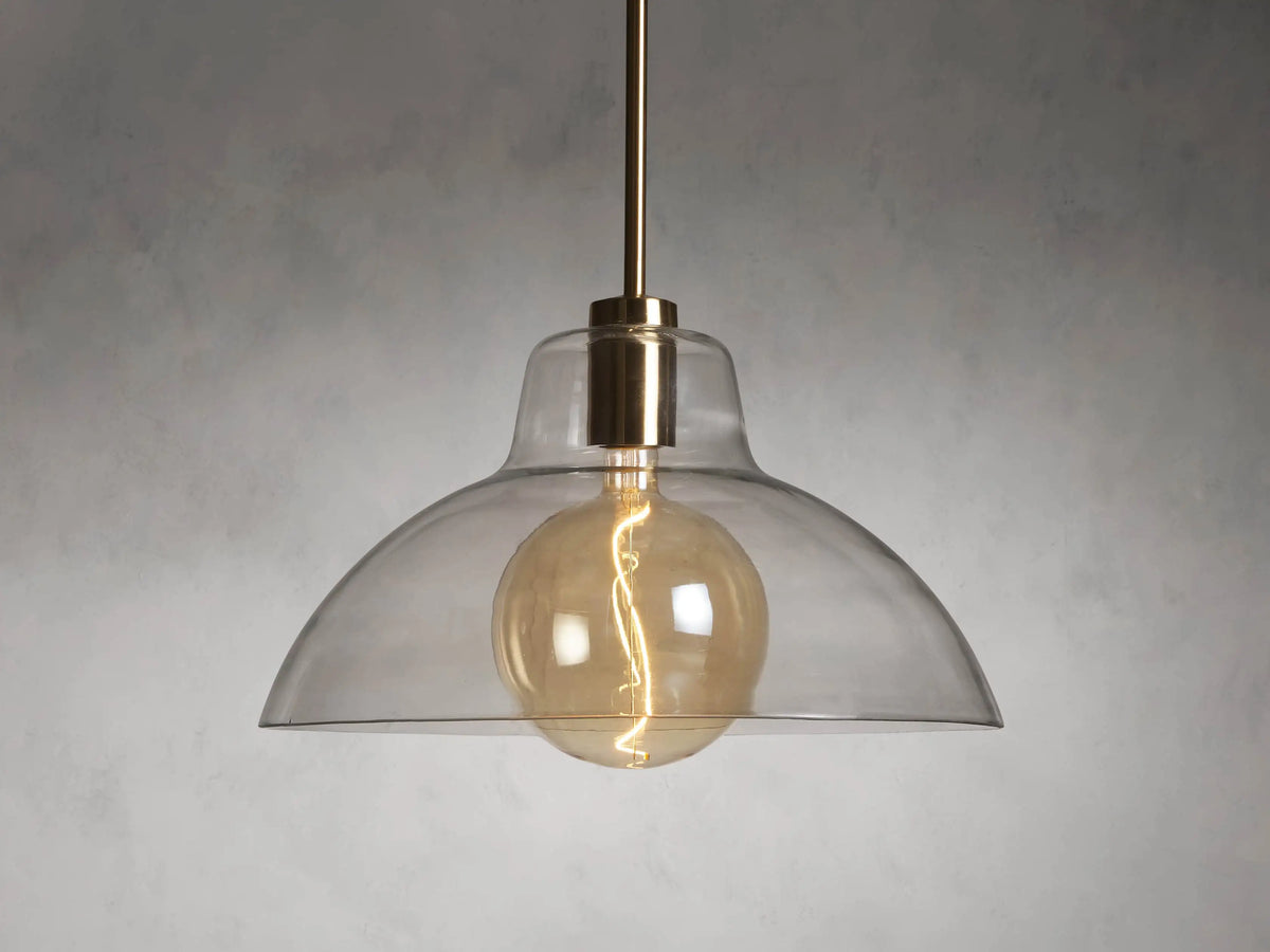 Bauer Dome Pendant with a transparent glass shade showcasing a glowing LED G200 bulb and brass finish, suspended by a rod.