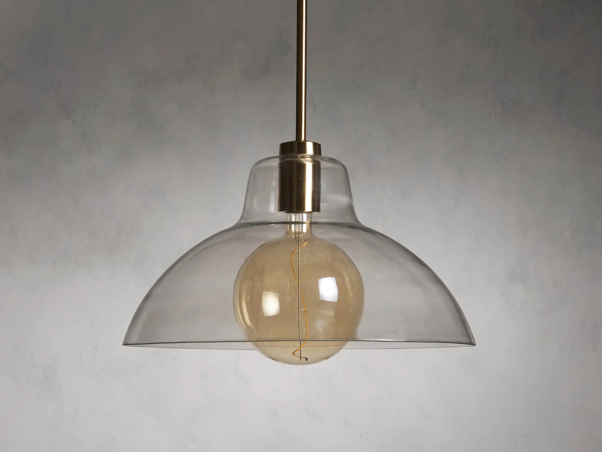 Bauer Dome Pendant with a transparent glass shade showcasing a glowing LED G200 bulb and brass finish, suspended by a rod.