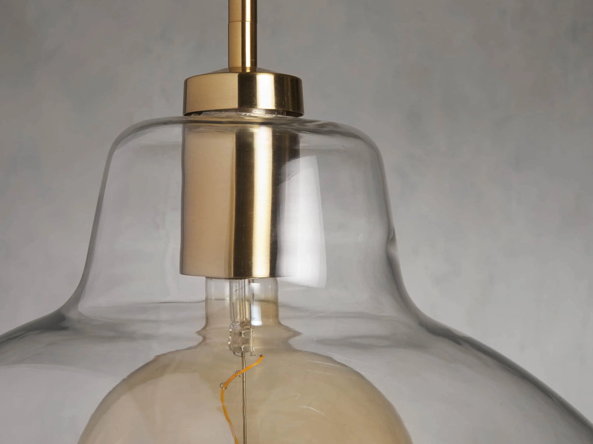 Bauer Dome Pendant with clear glass dome and visible LED bulb, brass finish, suspended from a pole against a neutral background.