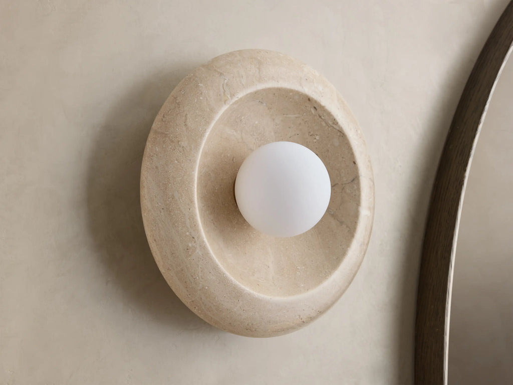 Front view of a round, light gray stone wall light with a warm ochre-colored concave interior and a glowing white bulb.