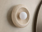 Front view of a round, light gray stone wall light with a warm ochre-colored concave interior and a glowing white bulb.