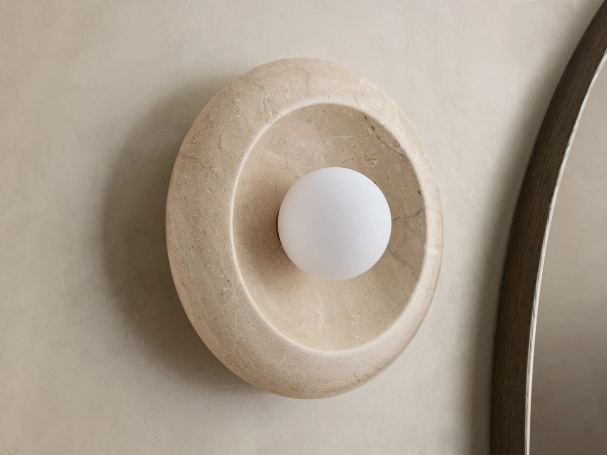 Front view of a round, light gray stone wall light with a warm ochre-colored concave interior and a glowing white bulb.