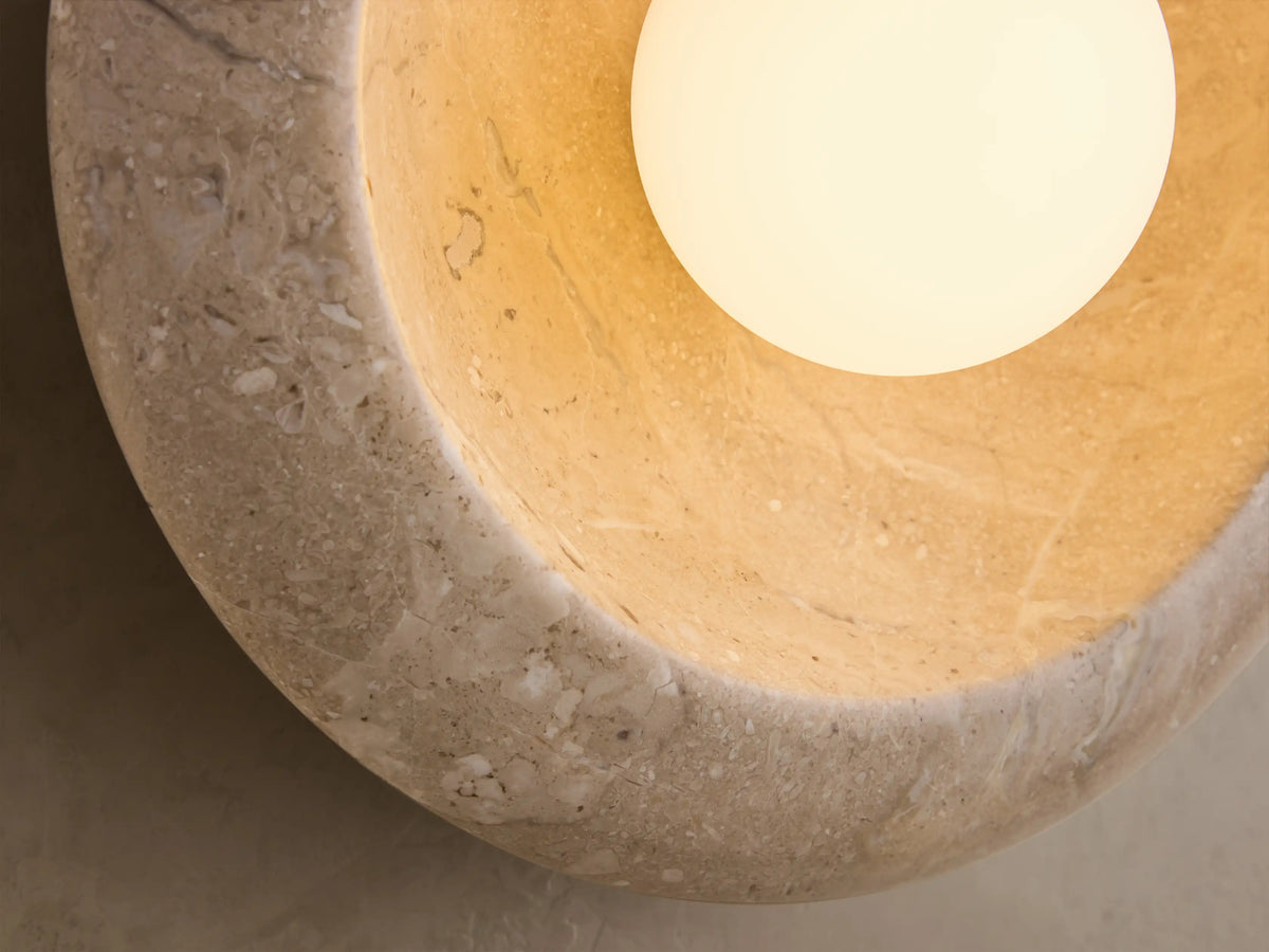 Front view of the beige Travertine Wall Sconce, a circular natural stone fixture with a white spherical bulb.