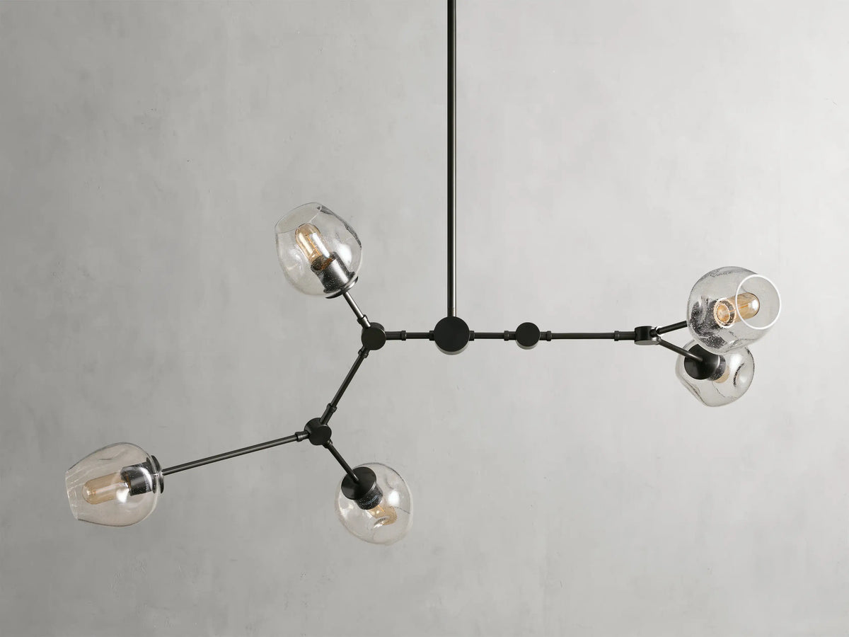 Noella Bronze Chandelier with five arms, clear glass bulb covers, and a sleek bronze finish against a light gray background.
