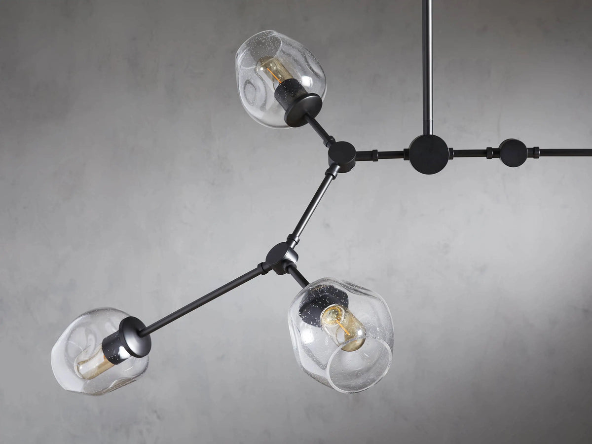 Noella Bronze Chandelier with five clear glass bulb holders on a bronze metal frame, hanging against a light gray wall.