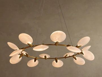 Warmly lit chandelier with a circular brass frame and multiple oval, translucent white diffusers with swirling patterns.
