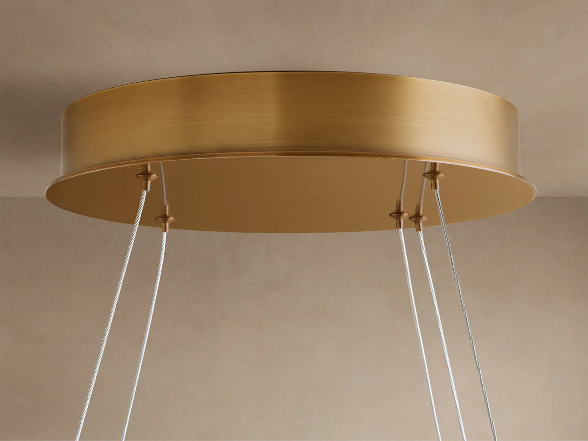 Warmly lit chandelier with a circular brass frame and multiple oval, translucent white diffusers with swirling patterns.