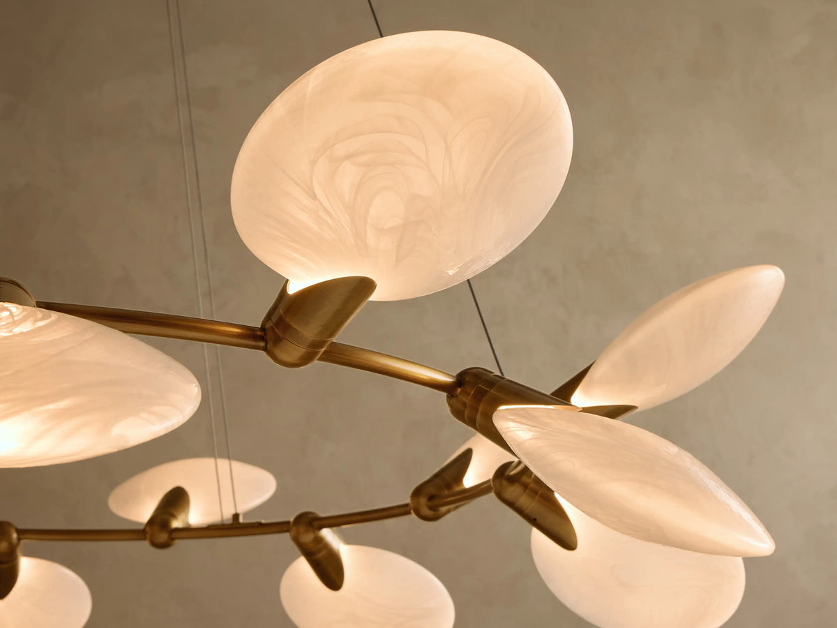 Gold-toned chandelier with a circular frame adorned with many oval milky white glass shades, suspended from above.
