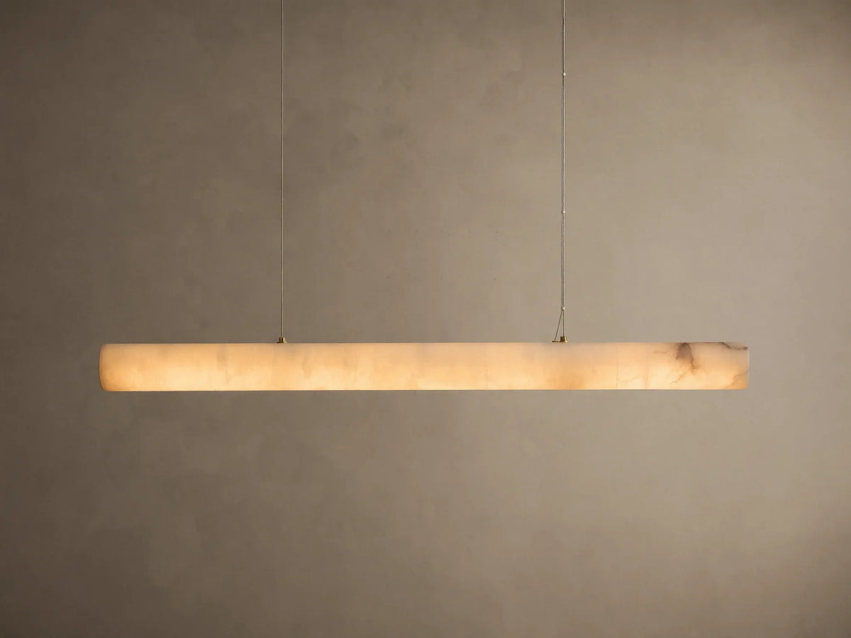 Translucent off-white onyx linear pendant light, glowing warmly with visible brown veining, suspended by thin wires.