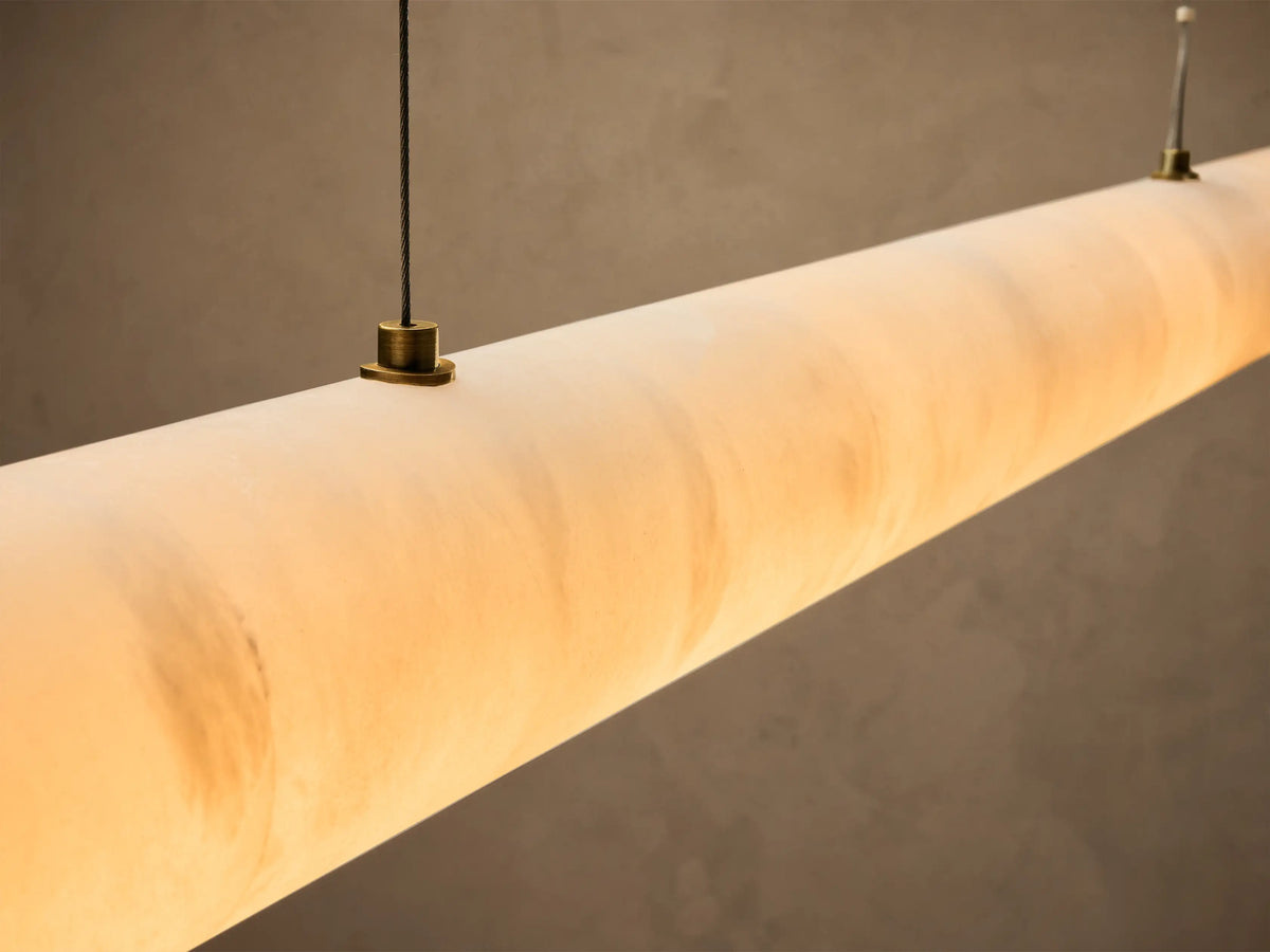 Close-up of a warm-glowing, cylindrical linear pendant light made of translucent material.