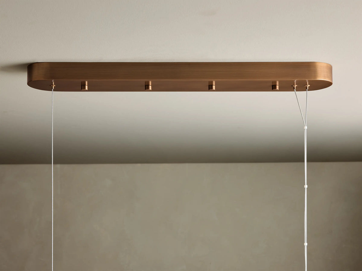 Close-up of a glowing, translucent linear pendant light with warm yellow-orange light, showing natural patterns and brass fittings.